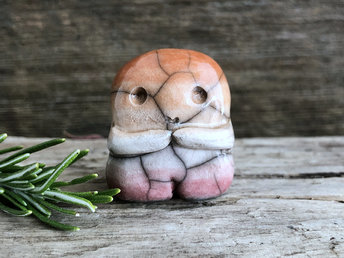A sweet little nature spirit ceramic guardian statue glazed in the lesbian flag orange, white, and pink colours and with a lovely, gentle face and little arms. It has a small branch design carved up one side.