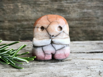 A sweet little nature spirit ceramic guardian statue glazed in the lesbian flag orange, white, and pink colours and with a lovely, gentle face and little arms. It has a small branch design carved up one side.