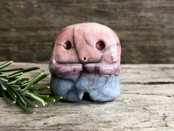 A sweet little nature spirit ceramic guardian statue glazed in the bisexual pink, purple, and blue colours and with a lovely, gentle face and little arms. It has a small branch design carved up one side.