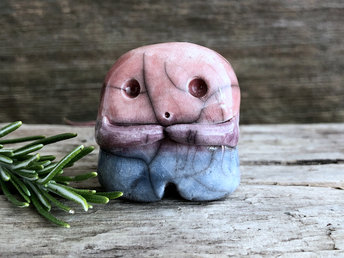 A sweet little nature spirit ceramic guardian statue glazed in the bisexual flag pink, purple, and blue colours and with a lovely, gentle face and little arms. It has a small branch design carved up one side.