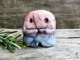 A sweet little nature spirit ceramic guardian statue glazed in the bisexual flag pink, purple, and blue colours and with a lovely, gentle face and little arms. It has a small branch design carved up one side.