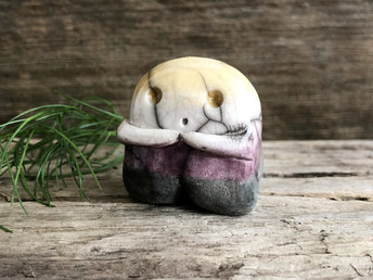 A sweet little nature spirit ceramic guardian statue glazed in the non-binary black, purple, white and yellow colours and with a lovely, gentle face and little arms. It has a small branch design carved up one side.