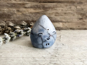 A small raindrop raku ceramic sculpture glazed in soft blues with a smiley face. A prayer to end the droughts and floods.