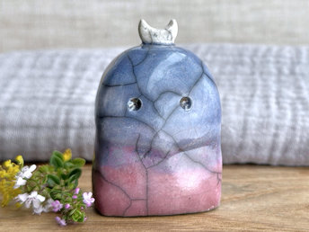 A kodama nature and forest spirit kami ceramic raku sculpture glazed in a bottom-to-top gradient of mauve to blue. It has a gentle face, and a white crescent moon on its head.