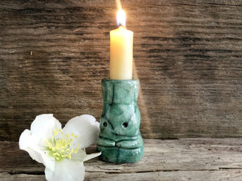 A sweet little kodama nature spirit ceramic candle holder glazed in shades of green and with a lovely, gentle face and little arms. The candlestick bit is on the top of it head.