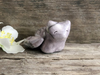 Raku ceramic kitsune fox glazed in grey-violet. She is lying down with her tail curled around her body, and she has a very gentle face.