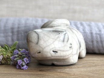 Little raku ceramic cat spirit kami sculpture glazed in white. It has a kind, gentle, sleepy face, and its tail is curled over its back on its right.