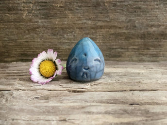 A very small raindrop raku ceramic sculpture glazed in blue and turquoise with a smiley face. A prayer to end the droughts and floods.