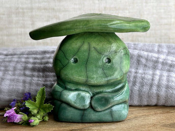 Raku ceramic sculpture glazed in a bottom-to-top gradient of forest green to spring green with a kind, but sad and worried face, and a spring green leaf on their head. They also have two cute little arms.
