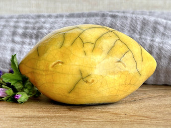 a very happy raku ceramic sculpture of a lemon. it's glazed in a golden yellow colour and has a kind, friendly face.