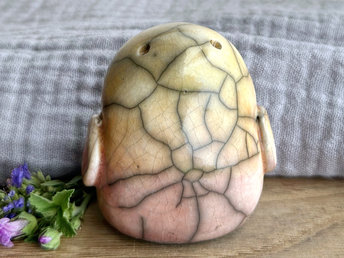 chonky raku ceramic bird sculpture glazed in a top-to-bottom gradient of pale golden yellow to pale peach to pale pinky red. it has a kind, gentle, and slightly concerned face and feels very reassuring to hold. it has two little wings at its sides folded flat to its body.