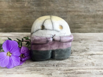 A sweet little nature spirit ceramic guardian statue glazed in the non-binary flag black, purple, white and yellow colours and with a lovely, gentle face and little arms. It has a small branch design carved up one side.