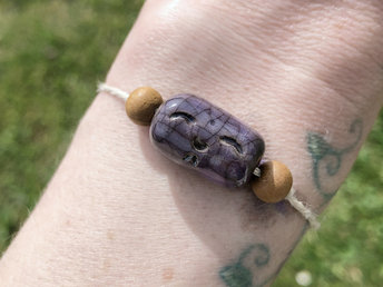 Violet-purple raku ceramic cylindrical Shinto Jizo bead bracelet with two ethical sandalwood beads. It is strung on an adjustable eco-hemp cord. Jizo looks very happy and kind!