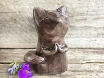 Raku ceramic fox sculpture with a kind, gentle face and sweet praying hands. It is glazed in a warm brown colour, and its tail is curled around its body.
