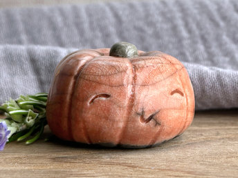 Raku ceramic orange pumpkin nature spirit kami sculpture with a very happy, smiley face. It has a small green-brown stem at the top.