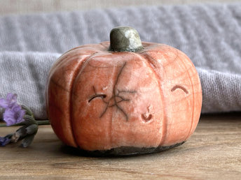 Raku ceramic orange pumpkin nature spirit kami sculpture with a very happy, smiley face. It has a small green-brown stem at the top.