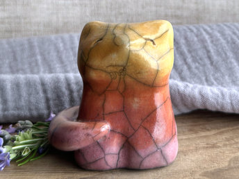Raku ceramic sitting fox glazed in a gradient from mauve to orange to golden yellow (bottom to top). It has a kind face, and its tail is curled around its body on its right side.