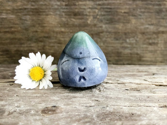A small raindrop raku ceramic sculpture glazed in blue and aqua green (bottom to top) with a smiley face. A prayer to end the droughts and floods.