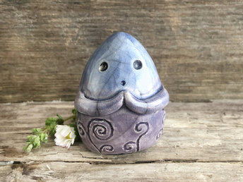 vaguely dome-shaped nature spirit ceramic sculpture. it is glazed in a bottom-to-top gradient of violet to blue and has spiral carvings on its body. it also has a gentle face, and two little arms across its front.