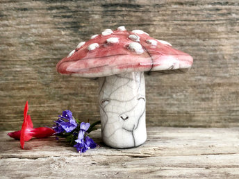 Cute raku ceramic fly agaric mushroom sculpture. Its stalk (where its smiley face is) is a creamy white colour, and its mushroom cap is a deep red with textured white bumps.
