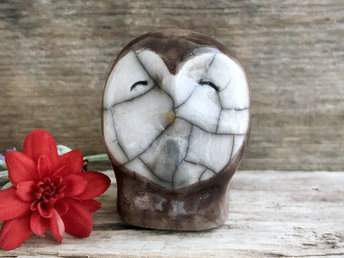 Ceramic raku owl kami nature spirit sculpture glazed mostly in brown with a white heart-shaped face. It has a pale yellow beak and a very kind, friendly expression.