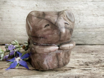 raku ceramic sculpture of a sweet little mouse. it's glazed in warn brown with a hint of mauve on the left side. it has two cute little arms, a happy, gently smiling face, and a long tail curled up on its back.