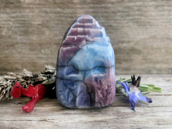 Tiny raku ceramic cottage glazed in pale blue, violet, and turquoise. Its roof is glazed in grey and carved to look like slates. It has a carved door and windows and lots of plant and flower carvings too.