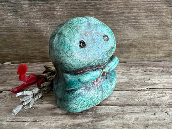A kodama nature spirit ceramic guardian statue glazed in a turquoise and copper glaze. It has a wide face, two big eyes, and cute little arms.