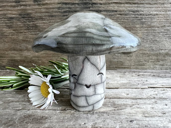 Cute mushroom raku ceramic sculpture with a very smiley face. His stalk is glazed in creamy-white (this is where his face is) and his mushroom cap is grey-brown.