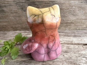 Raku ceramic sitting fox glazed in a gradient from mauve to orange to golden yellow (bottom to top). It has a kind face, and its tail is curled around its body.