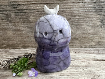 A kodama nature and forest spirit kami ceramic raku sculpture glazed in a bottom-to-top gradient of darker to slightly lighter violet. It has a gentle face, and a white crescent moon on its head.