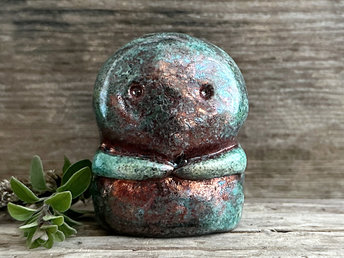 A kodama nature spirit ceramic guardian statue glazed in a turquoise and copper glaze. It has a wide face, two big eyes, and cute little arms.