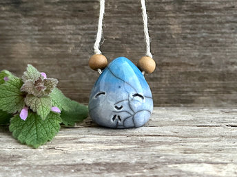raku ceramic pendant in the shape of a tiny raindrop with a happy face. it's glazed in a gradient from blue to aqua-turquoise (bottom to top) and strung on an eco flax cord. there is a round sandalwood bead on either side of the pendant.