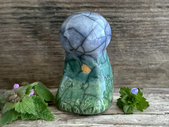 Raku ceramic mother earth spirit spirit sculpture glazed in spring green, forest green, and blue (bottom to top). It has plant shapes and flowers carved into it and a yellow sun carving too.