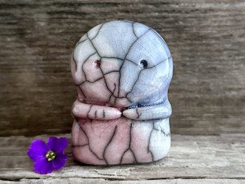 A kodama nature spirit ceramic guardian statue glazed in the pink, blue, and white of the transgender pride flag. It has a wide face, two big eyes, and cute little arms.
