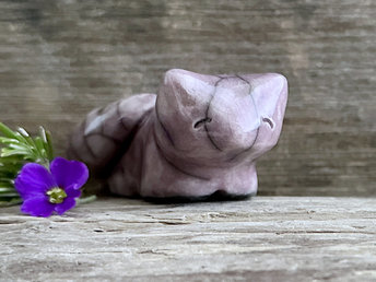 Raku ceramic kitsune fox glazed in pale purple. It is lying down with its tail curled around its body, and it has a very gentle face.