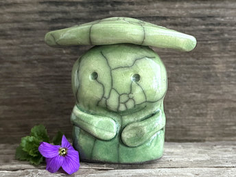 Raku ceramic sculpture glazed in spring green colours with a sweet face and a lighter, yellow-green leaf on its head. It also has two cute little arms.