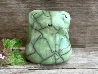 a happy green frog raku ceramic sculpture. it has a smiley face and is a lovely shape to hold in the hand.