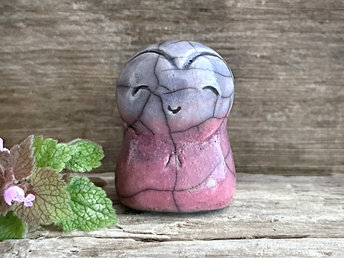 A smiley and loving Jizo Shinto raku ceramic sculpture talisman glazed in a bottom-to-top gradient of mauve to pale indigo blue. She has a heart shape around her kind, gentle face and is a wonderful shape to hold in the hand.