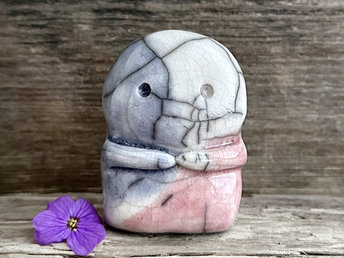 A kodama nature spirit ceramic guardian statue glazed in the pink, blue, and white of the transgender pride flag. It has a wide face, two big eyes, and cute little arms.