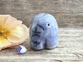 a small and stout nature spirit raku sculpture glazed in blue. it has a cute little face, and a little plant carving on its right side.