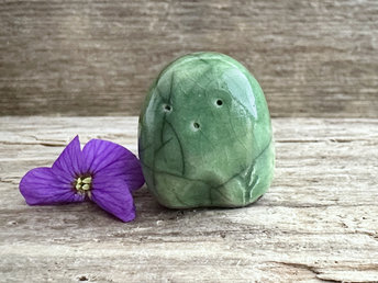 a small and stout nature spirit raku sculpture glazed in green. it has a cute little face, and a little plant carving on its left side.