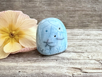 a small and stout nature spirit raku sculpture glazed in turquoise. it has a cute little face, and little plant carvings around its base.
