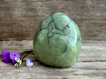 raku ceramic nature spirit sculpture glaze in a bottom-to-top gradient of spring green to a slightly more bluey green. it's very round but slightly pointy on top and it has a cute and happy wee face.