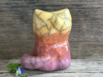Raku ceramic sitting fox glazed in a gradient from mauve to orange to golden yellow (bottom to top). It has a kind face, and its tail is curled around its body.