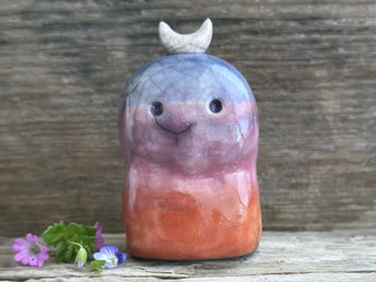 A kodama nature and forest spirit kami ceramic raku sculpture glazed in a bottom-to-top gradient of burnt red-orange to mauve to purple to indigo. It has a gentle face, and a white crescent moon on its head.