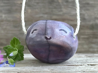 raku ceramic violet-mauve colour "worry stone" pendant with a happy little face at the top.