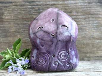 a nature spirit sculpture shaped a bit like a wide hourglass that's a little pointy at the top. it is glazed in a bottom-to-top gradient of violet-purple to soft mauve and has spiral carvings on its body. it also has a gentle, happy face.