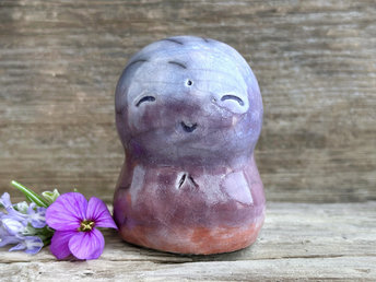 A smiley and loving Jizo Shinto raku ceramic sculpture talisman glazed in a bottom-to-top gradient of burnt orange to mauve to violet-blue. It has a kind, gentle face and is a wonderful smooth shape to hold in the hand.