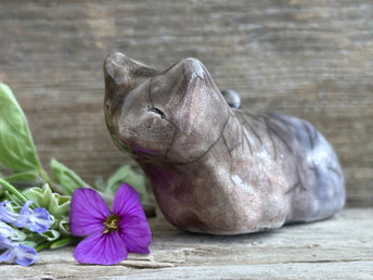 Raku ceramic kitsune fox glazed in a head-to-tail gradient of brown to pale violet. It is lying down with its tail curled over its back, and it has a very gentle face.